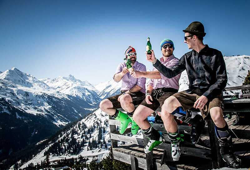 Drei Skifahrer in Lederhosen vor der Skihütte